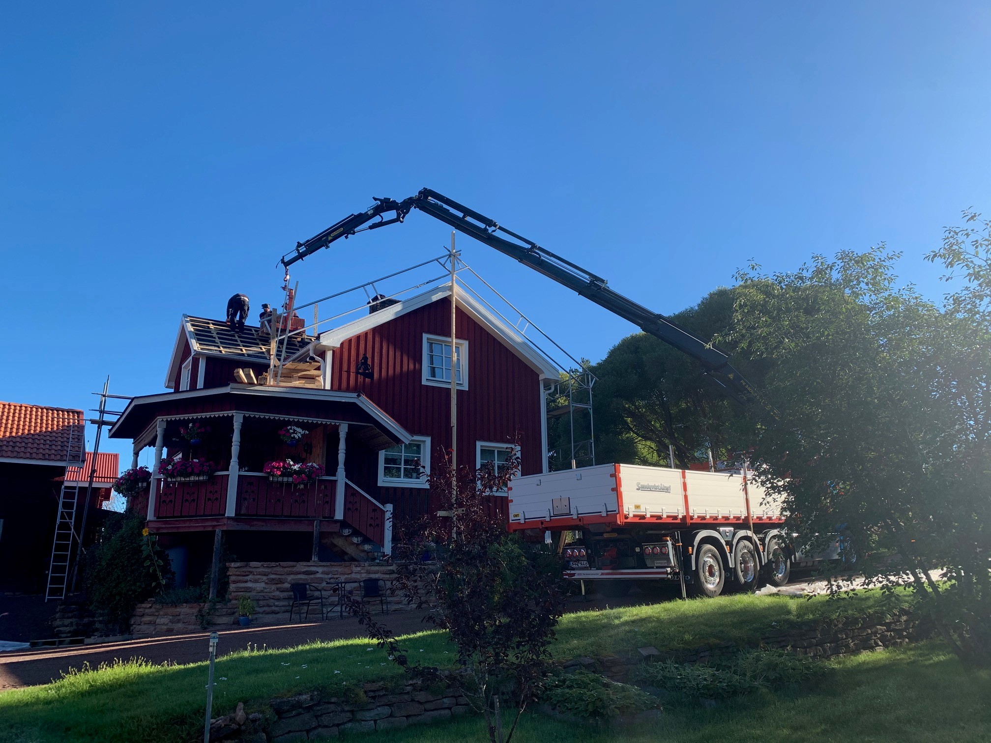 Kranbil levererar takmaterial till ett takbyte på ett rödmålat hus