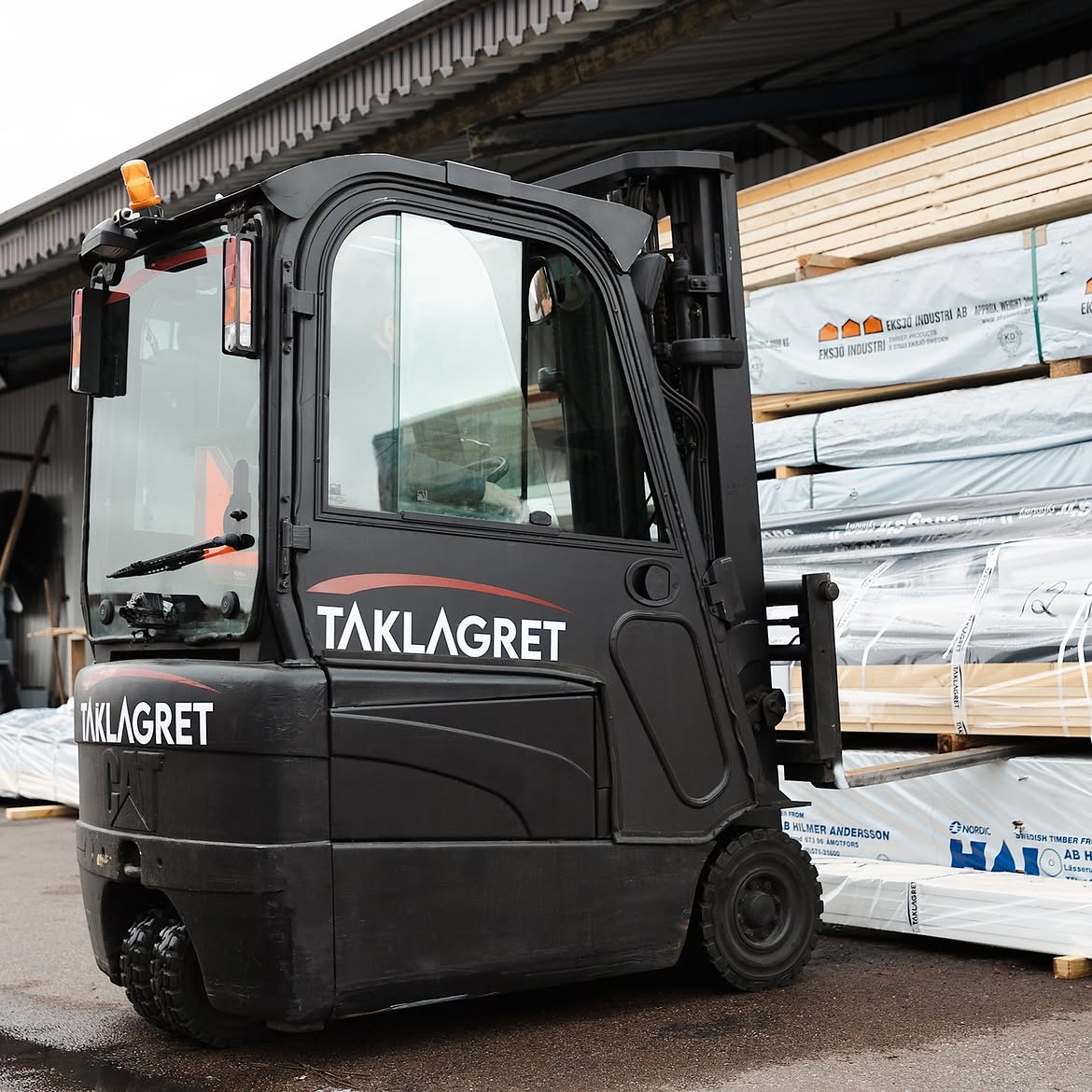 Motviktstruck med Taklagrets logotyp i lagret framför paket med virke
