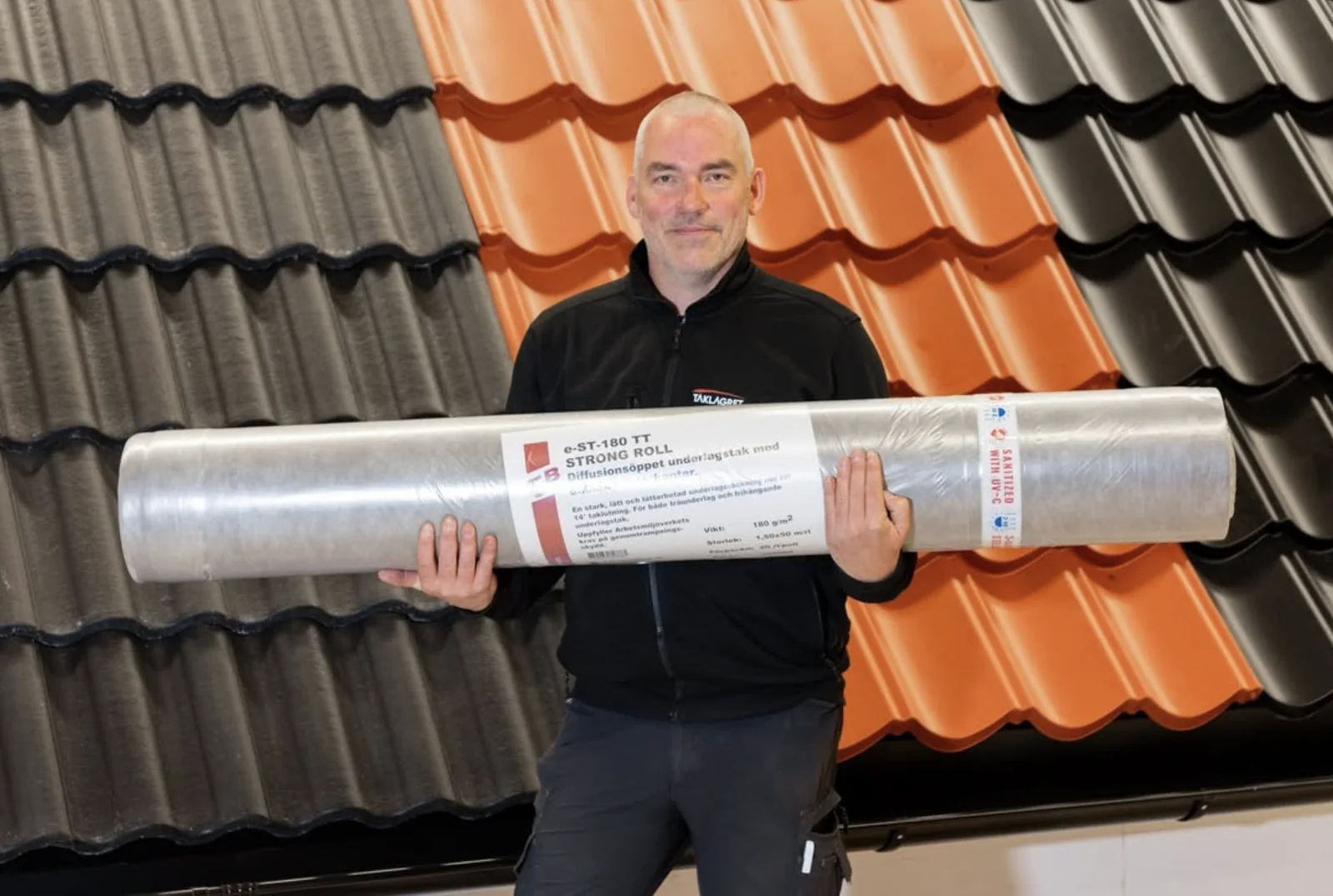 Medarbetare från Taklagret med en rulle TJB Strong Roll underlagstak framför takpannor